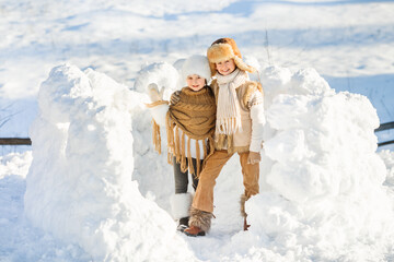 Fototapeta na wymiar Happy family have fun playing in snow fort on sunny winter day. Smiling children pose looking at the camera. Beautiful winter vacation.