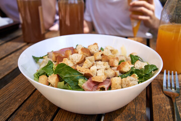 Caesar salad with croutons, lettuce, bacon and chicken on a wooden table outdoors