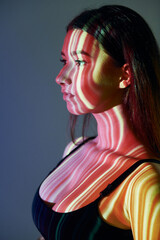 Yellow and red colored lines. Beautiful young woman is in projector neon lights in the studio