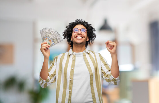 finance, currency and people concept - happy man holding hundreds of dollar money banknotes celebrating success over office background