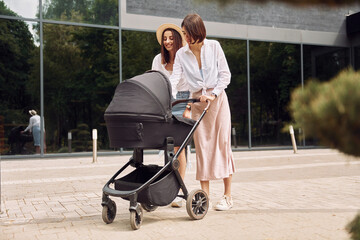 Two female friends having a walk with baby carriage outdoors