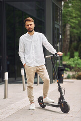 Posing for a camera. Stylish man is with his scooter outdoors at daytime