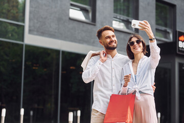 Making selfie. Beautiful couple have a shopping day outdoors at daytime