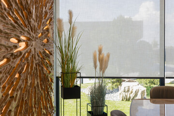 Roller blinds in the interior. Automatic solar shades large size on the window. Modern interior with wood decor panel on the wall. Green plants in hi-tech flower pots. Electric curtains for home.  - obrazy, fototapety, plakaty