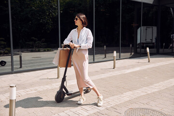 In sunglasses. Beautiful young woman is with her scooter outdoors