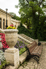 A beautiful stone flowerpot with bright flowers, a wooden bench and a staircase of the academic gallery in Pyatigorsk Russia among the lush green foliage of trees on a summer day