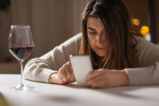 alcoholism, alcohol addiction and people concept - drunk woman or female alcoholic with smartphone drinking red wine at home