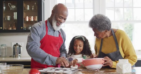 Video of happy african american granddaughter baking with grandparents in kitchen - Powered by Adobe