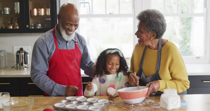 Video of happy african american granddaughter making cakes with grandparents in kitchen