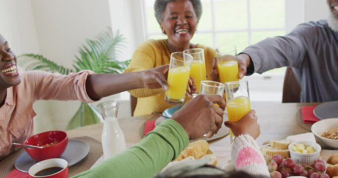 Video of happy african american parents, daughter and grandparents making a toast at dinner table