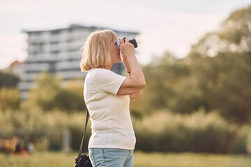 Photographer with a camera. Senior woman having nice weekend outdoors on the field at sunny day