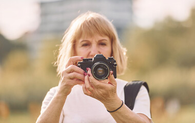 Using the camera. Making the photos. Senior woman having nice weekend outdoors on the field at sunny day