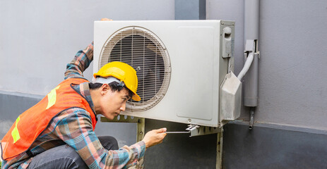 The air conditioner technician Uses a wrench to tighten the nut of the air compressor. Young Asian man repairman checking an outside air conditioner unit.