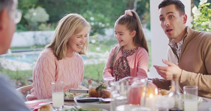 Video of happy caucasian father, daughter and grandparents talking at outdoor dinner table