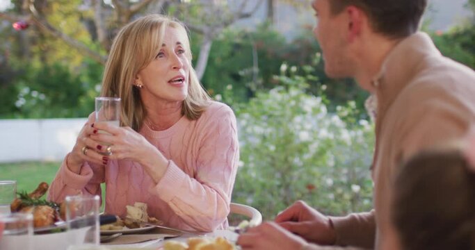 Video of happy caucasian senior mother and adult son talking at outdoor family dinner table