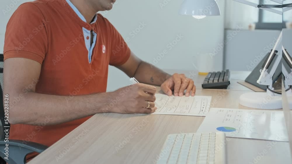Wall mural cropped slowmo of unrecognizable man signing business documents while sitting by computer at office 