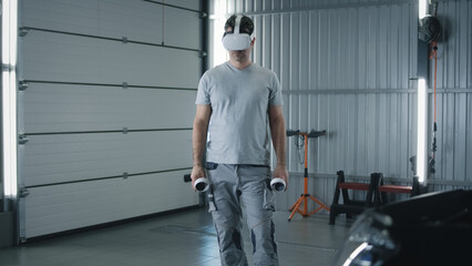 Fototapeta premium Man worker in uniform in a modern virtual reality glasses with controllers checking and testing a car after repairing in a car service