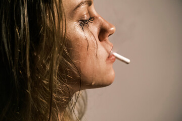 Fototapeta premium Crying young woman with cigarette in her mouth. Portrait of side view of unhappy woman experiencing an emotional crisis in her life. Domestic psychological and physical violence