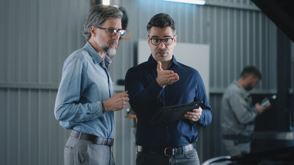 Manager in casual clothes with a tablet talking to a male client in a car service and discussing...