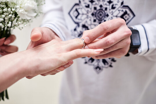 Close up picture of bride and groom's hands putting on a wedding ring at official marriage ceremony. Bride and groom are getting married at city hall. National ukrainian embroidered costumes