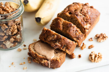 Vegan banana bread loaf with walnuts cut into slices on a marble board, closeup view