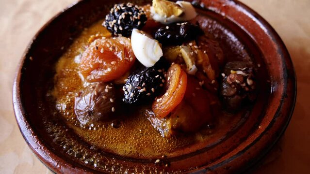 A  traditional beef meat tajine, tagine, meal served in a Moroccan clay pot, hot, and sizzling. Traditional Moroccan slow-cooked meal with beef, plums, appricot, nuts, and eggs. 4k food background.