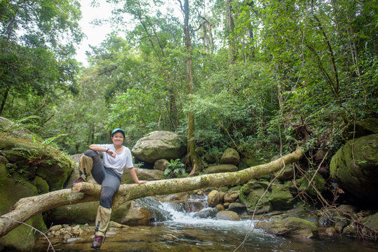 A female tourist sits on a log in the middle of a lush forest.