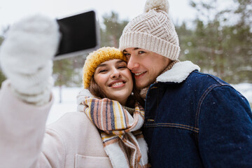 season, technology and leisure concept - happy couple with smartphone taking selfie in winter park