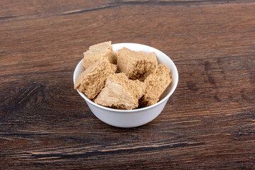 Pieces of sunflower halva in a white porcelain bowl on a wooden background.