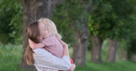 Happy woman holding little girl and hugs her outdoors. Young mother with blonde daughter in each other embrace
