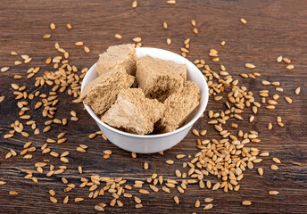 Sunflower halva chopped into pieces in a white porcelain bowl with sunflower seeds around the bowl.