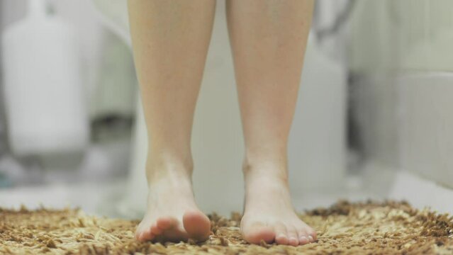 Woman is sitting on the toilet in the home bathroom. Legs close-up. Concept of constipation and diarrhea.