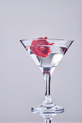 Vertical shot of cocktail with red flower. Transparent alcoholic drink.