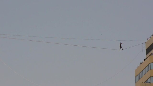 Brave man walks on tightrope stretched between twin towers. Slackline or Skywalk. Human keeps balance on top.