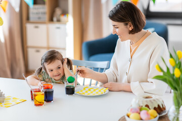 holidays, family and people concept - happy mother and little baby daughter dyeing easter eggs with colors at home