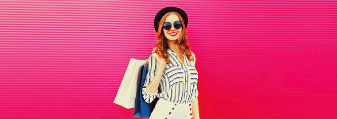 Portrait of beautiful smiling young woman with shopping bags wearing white striped shirt, summer black round hat on pink background, blank copy space for advertising text