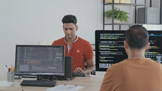 Waist up slowmo of Indian programmers typing program codes on computers in IT office