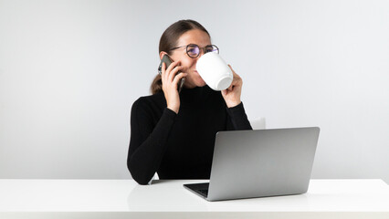 Woman at laptop talking on the phone and drinking coffee - workplace