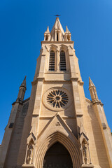 Fototapeta na wymiar Low angle view of the facade and bell tower of ancient St Anne or St Ann catholic church, a tourism landmark of Montpellier, France, on a blue sky summer afternoon