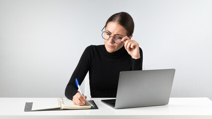 A serious businesswoman works in the office on a laptop, takes notes in a notebook