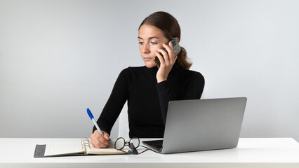 A phone call at the workplace - a woman at a laptop with a phone in the office