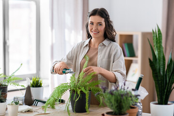 people, gardening and housework concept - happy woman cutting fern flower's leaves with pruner at home