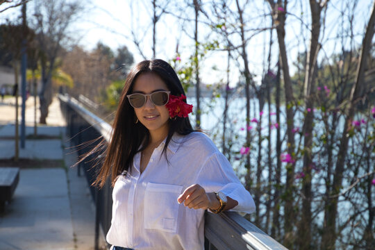 young and beautiful woman from south america touring europe. The woman is wearing a red flower in her hair and is leaning on the railing next to the river in sevilla. Travel and tourism concept.