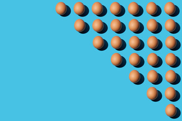 Trendy pattern of brown chicken eggs on a bright blue background with hard light and deep shadow. Minimal concept, diagonal copy space, close-up, top view.