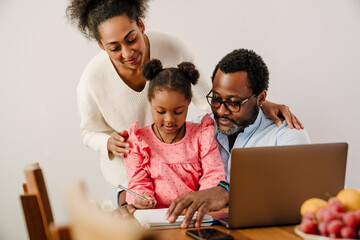 African american girl writing in notepad sitting with parents by table