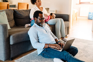 African american woman with daughter sitting on sofa, man using laptop