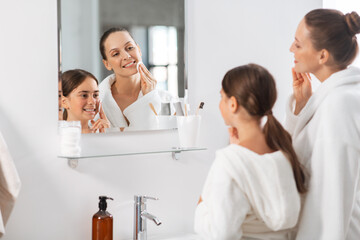 beauty, hygiene, morning and people concept - happy smiling mother and daughter with cotton pads cleaning face skin and looking to mirror at bathroom
