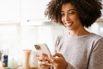 African american young woman smiling while using cellphone at home
