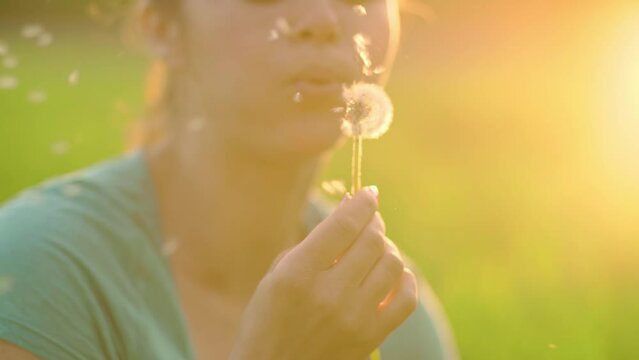 Beautiful girl blowing on a dandelion, fluff slowly flies through the air