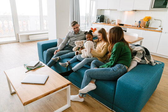 Happy family sitting on couch, adopted sisters playing stuffed toys
